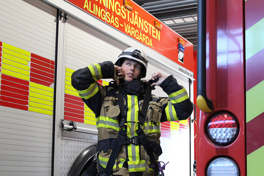 Kvinnlig brandman tar på sig sitt larmställ framför en brandbil