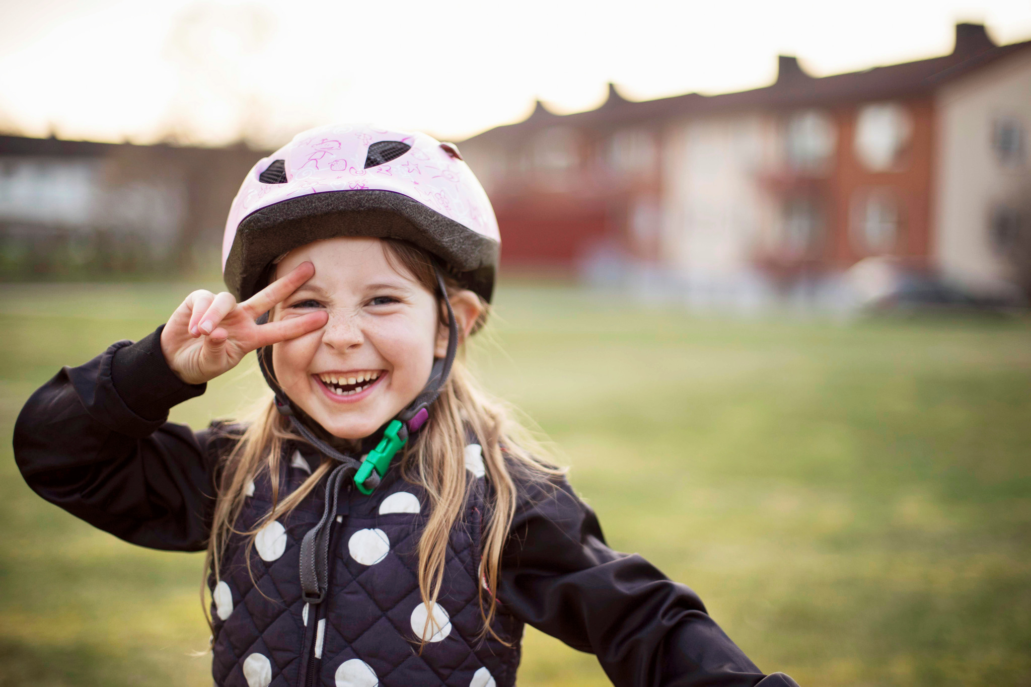 Flicka med cykelhjälm som gör ett liggande peacetecken framför ena ögat.
