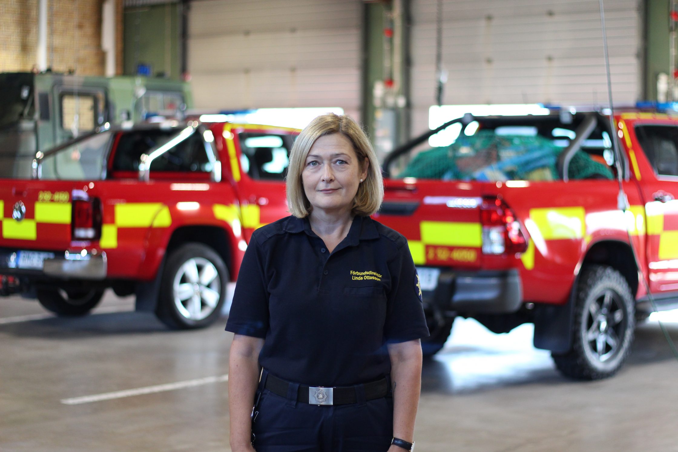 Linda Ottosson står i en hall framför två räddningstjänstbilar