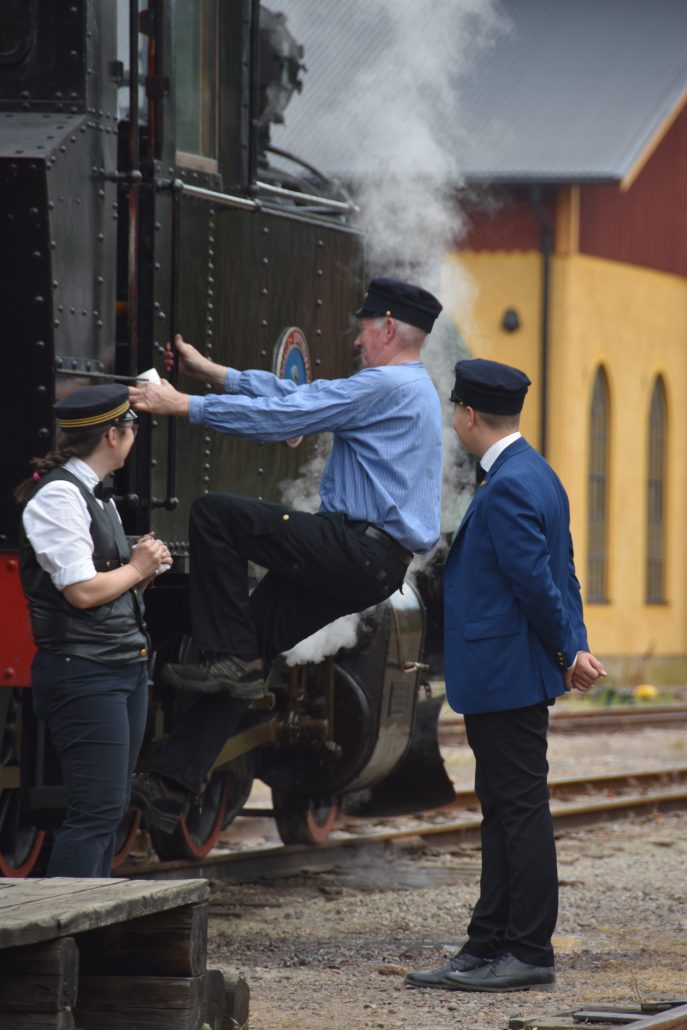 Lokförare och konduktör stiger ombord ett gammalt ånglok på Anten-Gräfsnäs Järnväg. 